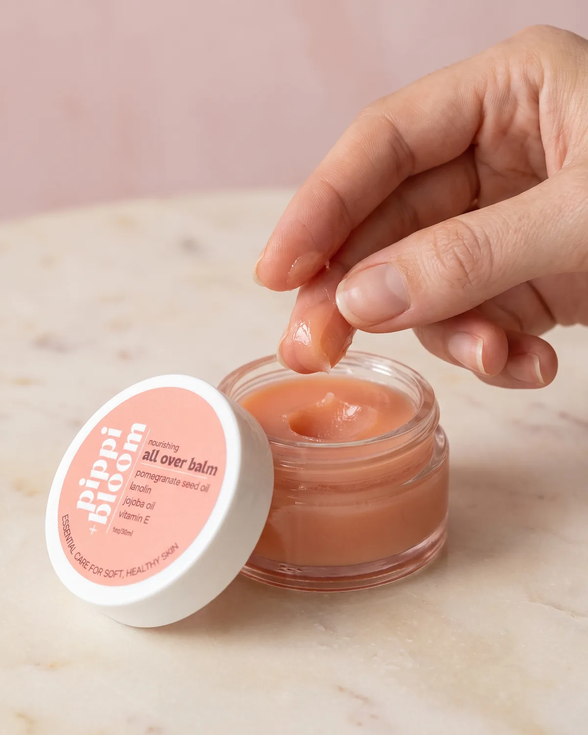 Fingertips lifting a little balm from the open jar and warming it between finger and thumb