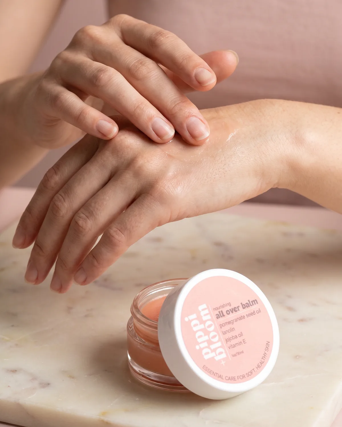 A thumb working balm into the knuckles of the other hand, the jar open behind
