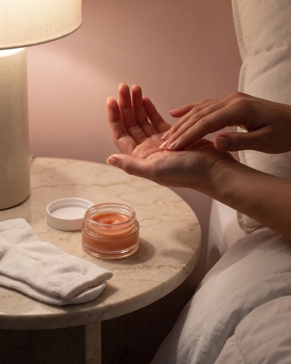 The jar on a nightstand in lamp light beside folded cotton gloves, a hand pulling one on