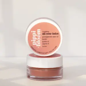 Pippi and Bloom all over balm — one jar open, one lid facing out — in window light against a pale wall