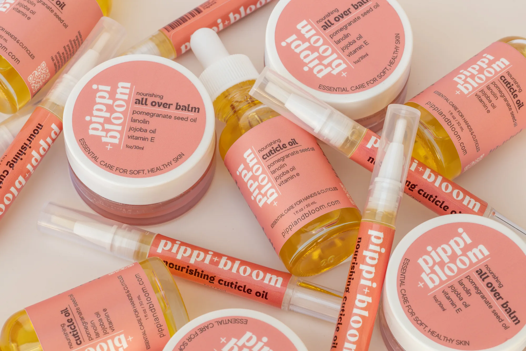 Cuticle oil droppers, brush pens and all over balm jars scattered together on a cream surface