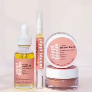 The full Pippi and Bloom line — cuticle oil dropper, brush pen, and all over balm — together in window light against a pale wall