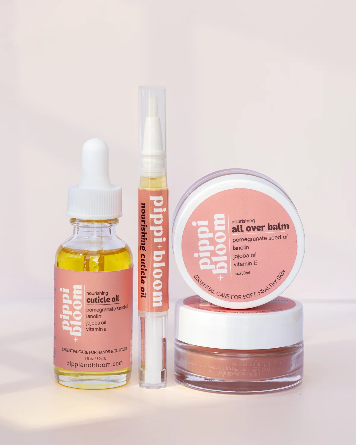 The full Pippi and Bloom line — cuticle oil dropper, brush pen, and all over balm — together in window light against a pale wall
