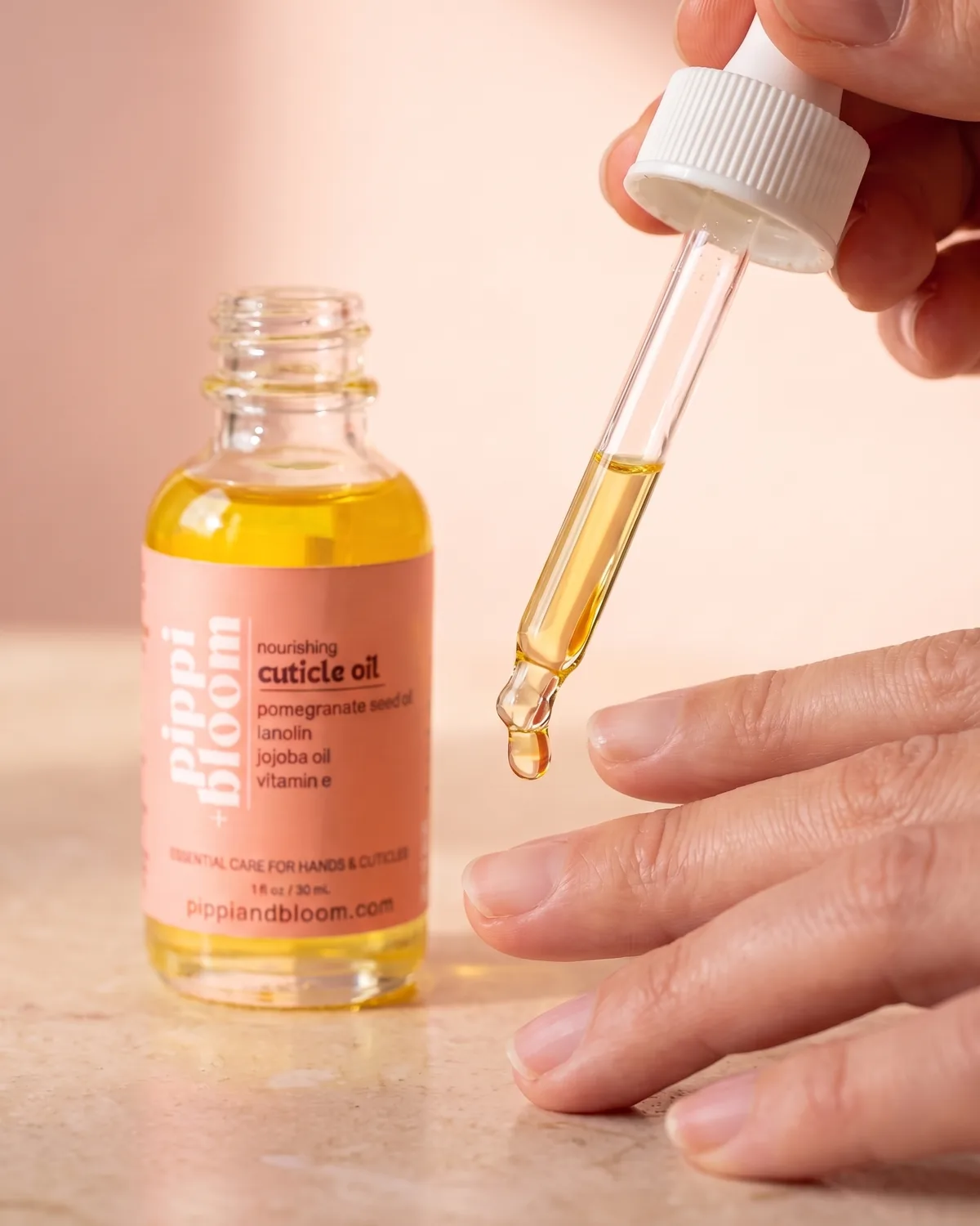A dropper holds a single bead of oil above a cuticle, the bottle beside it
